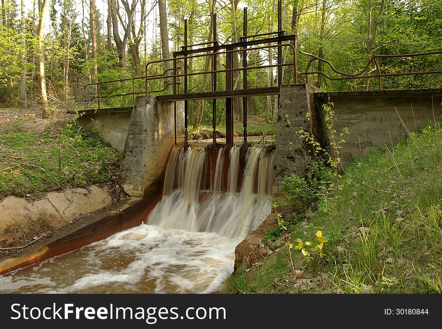 The photo shows a small dam, weir, located on a stream in the woods. The photo shows a small dam, weir, located on a stream in the woods.