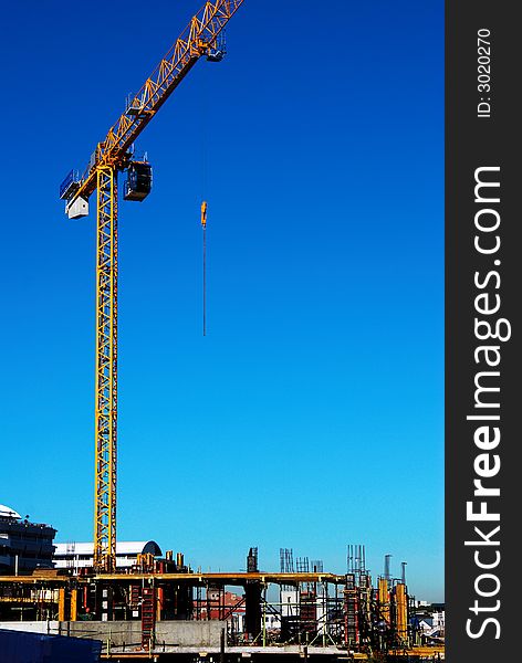A yellow construction crane on a constuction site with the lifting cable hanging in mid air