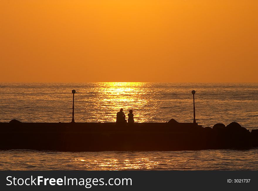 Romantic couple sitting on a pier and looking for sunset. Romantic couple sitting on a pier and looking for sunset