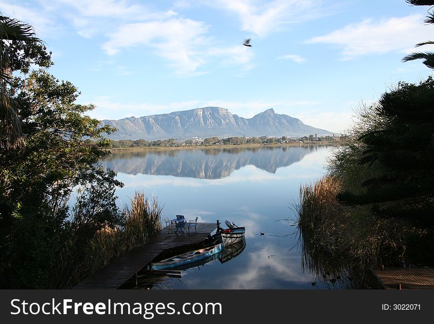 Still, windless day at Zeekoevlei, Cape Town. Reflection of Table Mountain and Devil's Peak with boats in foreground. Still, windless day at Zeekoevlei, Cape Town. Reflection of Table Mountain and Devil's Peak with boats in foreground.