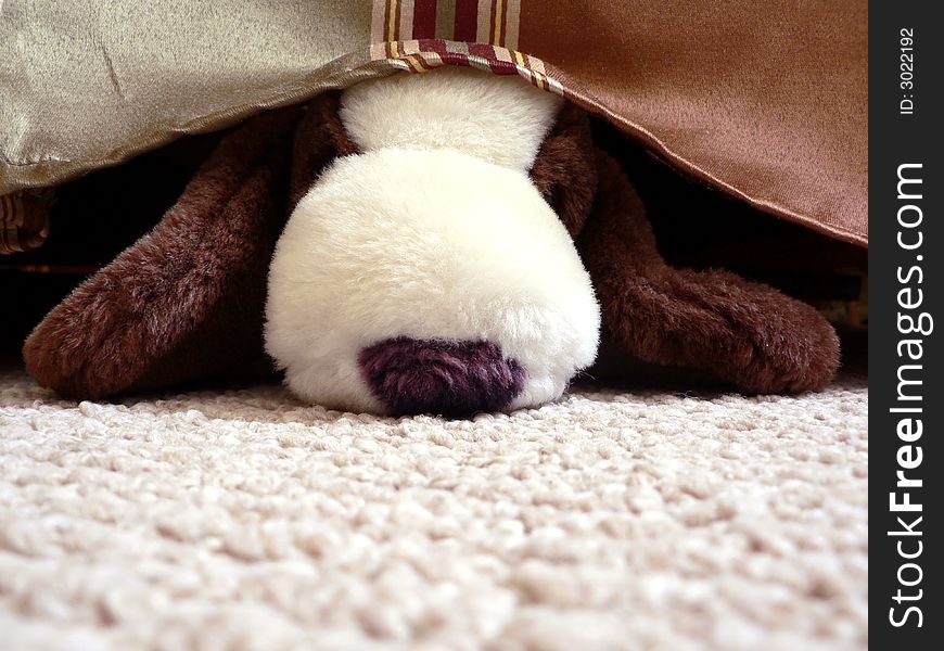 A stuffed toy dog hiding under a bed. A stuffed toy dog hiding under a bed
