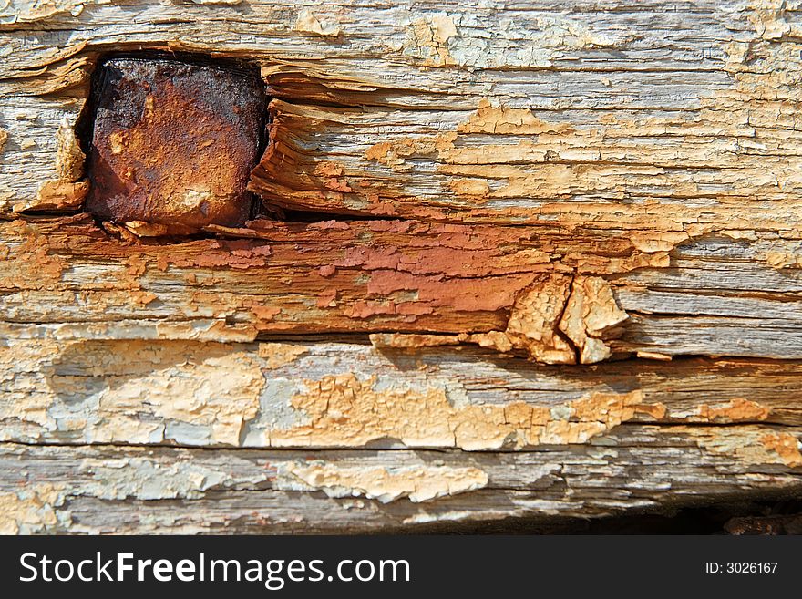 Some old painted and rusty boards in a boat cemetary with a large nail. Some old painted and rusty boards in a boat cemetary with a large nail