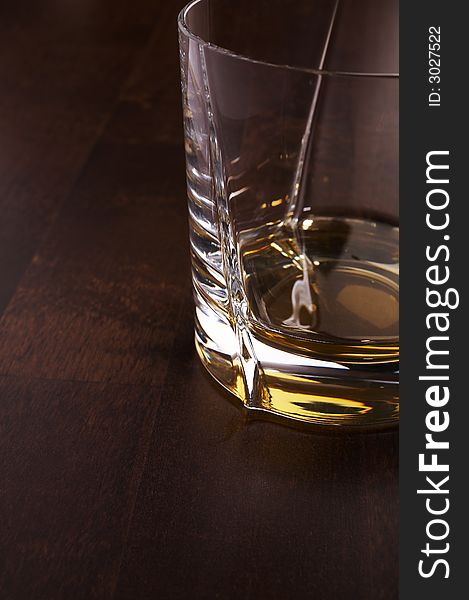 Part of the whiskey glass over a dark wooden table