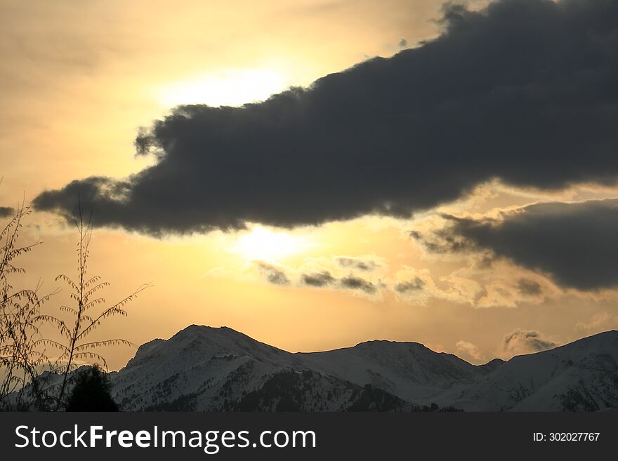 The Sun Behind A Dark Cloud Over The Snow-capped Mountains Of The Trans-Ili Alatau During Sunrise Behind Thickets Of Autumn Trees