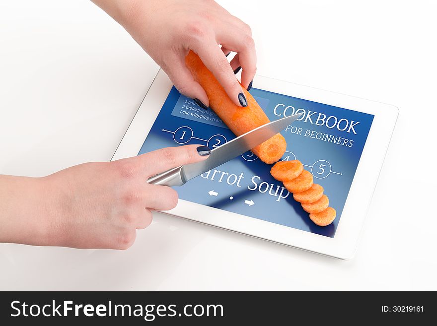 Women's hands is cutting the carrot on a tablet computer, on which there is a recipe of carrot soup. Women's hands is cutting the carrot on a tablet computer, on which there is a recipe of carrot soup.