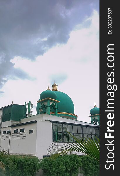 Nestled beneath Indonesia's expansive cloudy sky, a mosque stands as a serene testament to faith, its minarets reaching towards the heavens amidst the shifting clouds, embodying tranquility and spiritual devotion against the atmospheric backdrop. Nestled beneath Indonesia's expansive cloudy sky, a mosque stands as a serene testament to faith, its minarets reaching towards the heavens amidst the shifting clouds, embodying tranquility and spiritual devotion against the atmospheric backdrop.