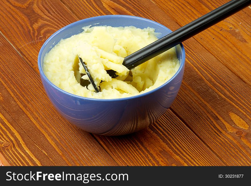 Tasty Mashed Potato with Potato Masher in Blue Bowl on Wooden background