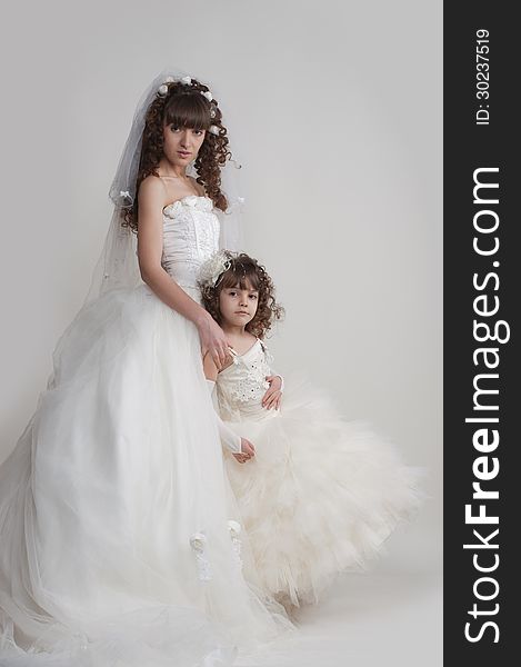 Full-length portrait of harmonious girl in a luxurious wedding dress with a cute little girl on a white background in the studio. Full-length portrait of harmonious girl in a luxurious wedding dress with a cute little girl on a white background in the studio