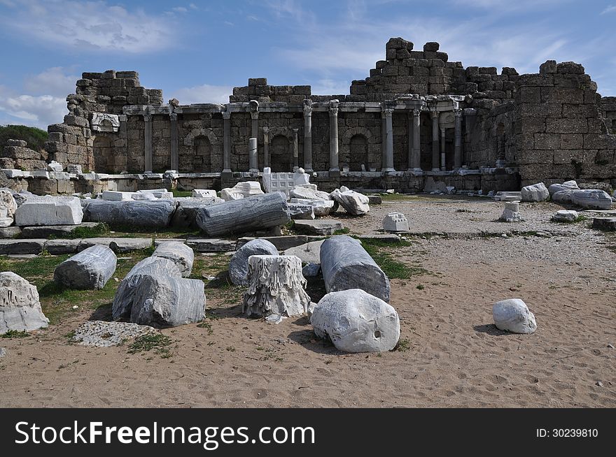 Image shows details of Antique Side, Turkey. Image is dominated by ruins in the front and in the middle. Sky is blue and light cloudy.
