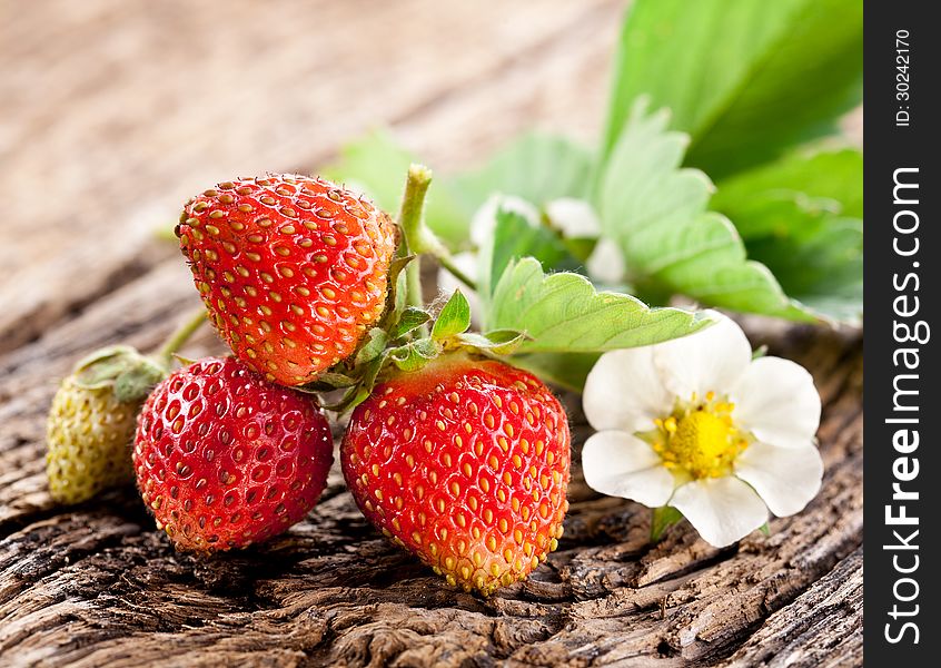 Strawberries with leaves on the old wooden table.