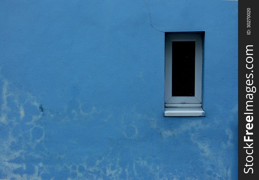 Small white framed window set into blue painted discoloured wall. Small white framed window set into blue painted discoloured wall