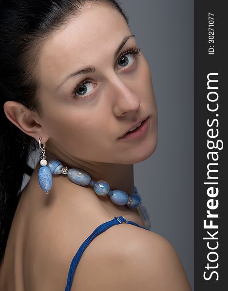 Close up portrait of beautiful face, long hair, brunette woman wearing charming light blue color earring and necklace, looking over shoulder. Shot in studio. Isolated on grey background. Close up portrait of beautiful face, long hair, brunette woman wearing charming light blue color earring and necklace, looking over shoulder. Shot in studio. Isolated on grey background.