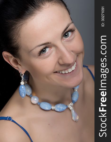 Close up portrait of young happy smiling woman wearing earrings and necklace of light blue stones. Natural beauty face. Selective focus. Shot in studio. Close up portrait of young happy smiling woman wearing earrings and necklace of light blue stones. Natural beauty face. Selective focus. Shot in studio.