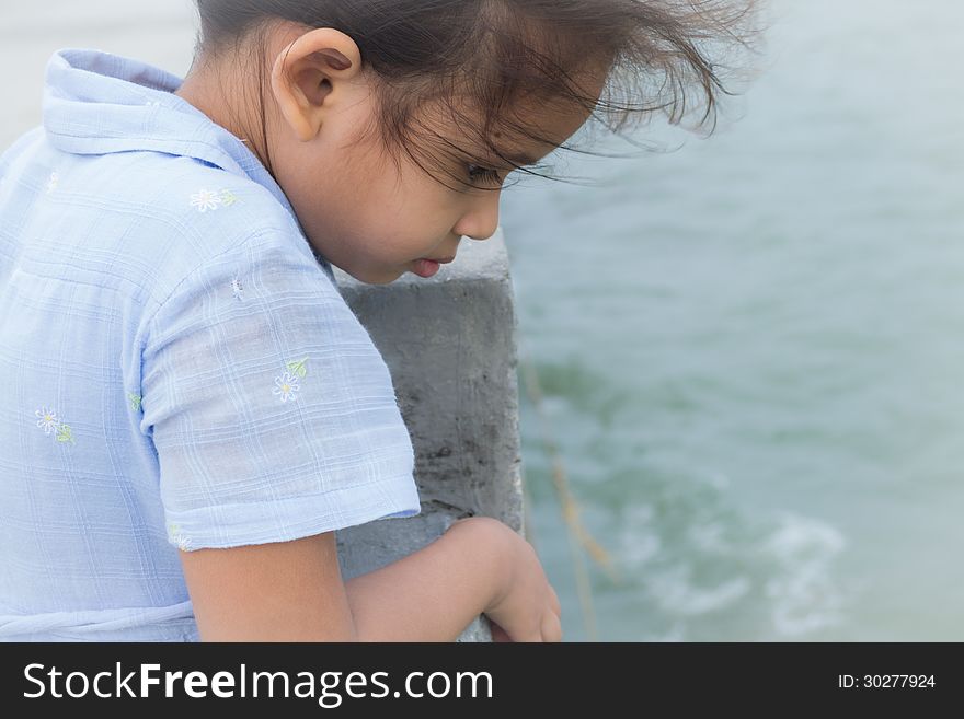 A cute girl is staring to the sea on a bridge with strong wind