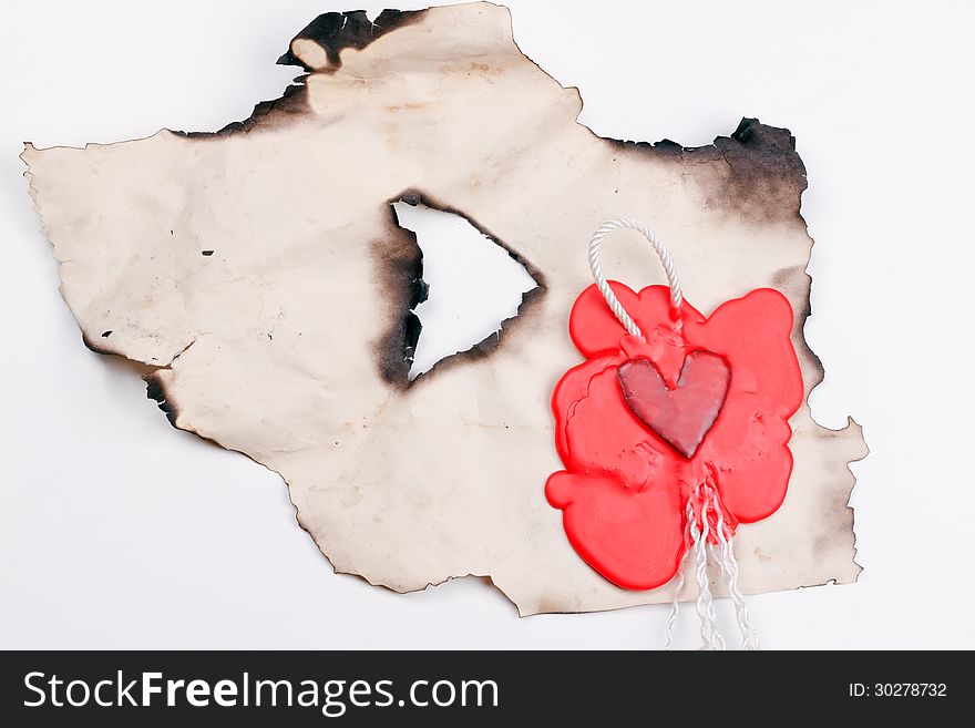 Mark in the shape of a heart made of red wax on a piece of burnt paper