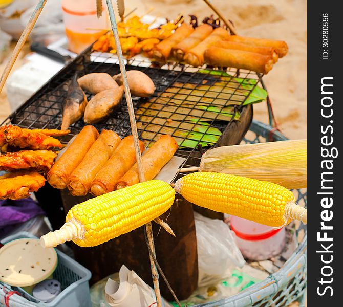 Traditional Thai food at small market on beach. Spring rolls, curry chicken and corn on grill