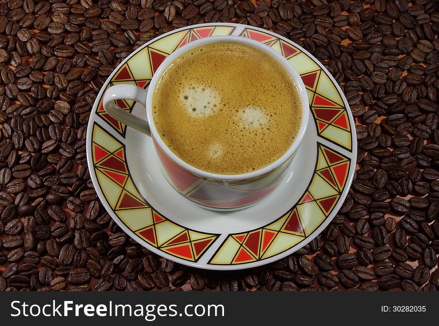 The photograph shows a porcelain espresso cup, standing on a porcelain saucer. The background for the cup and saucer are scattered coffee beans. The photograph shows a porcelain espresso cup, standing on a porcelain saucer. The background for the cup and saucer are scattered coffee beans.
