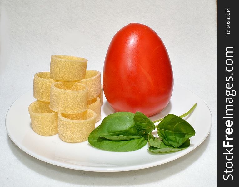 A tomato and basil and pasta on a plate. A tomato and basil and pasta on a plate.