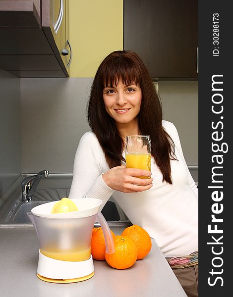 Smiling woman making and drinking orange juice in kitchen. Smiling woman making and drinking orange juice in kitchen