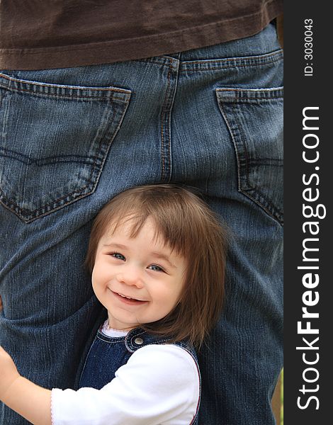 Young girl smiling and holding onto her fathers leg. Young girl smiling and holding onto her fathers leg.