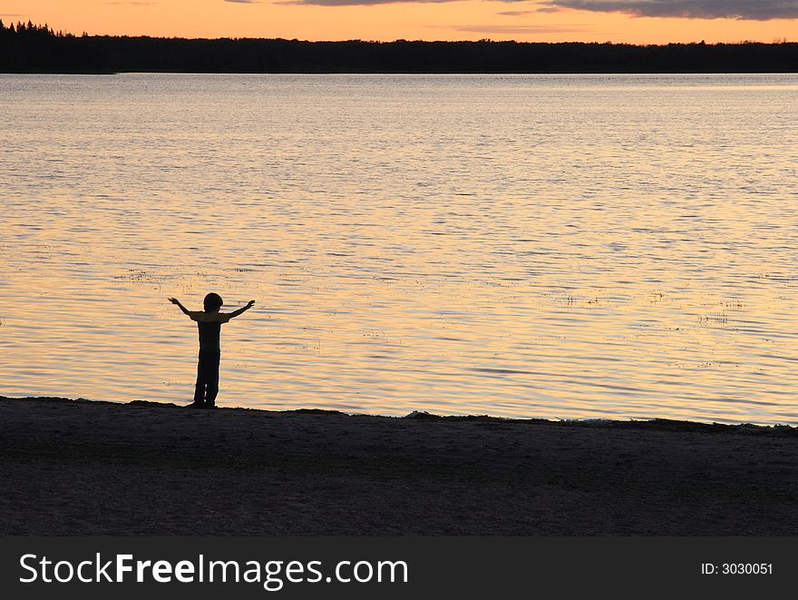 Young boy silhouetted against lake shore at sunset. Young boy silhouetted against lake shore at sunset.