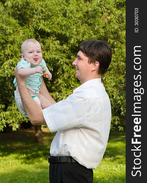 Father holds on hands of the small child on a background of green foliage. Father holds on hands of the small child on a background of green foliage