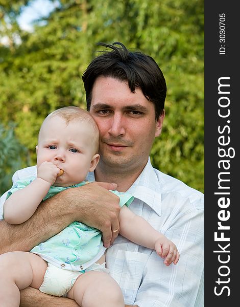 Father holds on hands of the small child on a background of green foliage. Father holds on hands of the small child on a background of green foliage