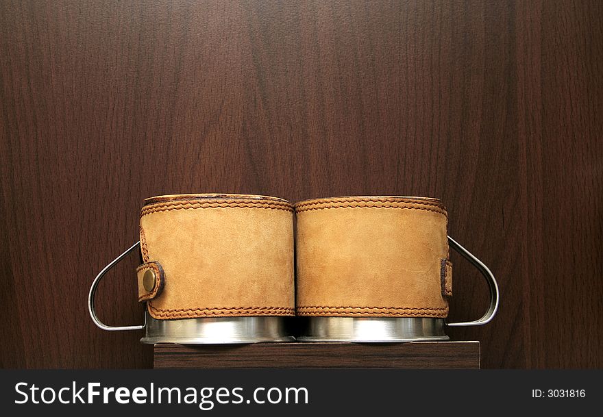 Two silver coffee mugs covered with leather on a brown background