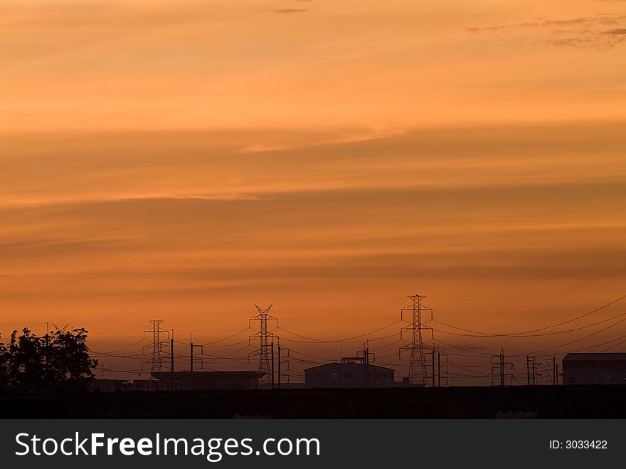 Sunrise in an industrial setting, with the sillhouettes of power lines and industrial buildings. Sunrise in an industrial setting, with the sillhouettes of power lines and industrial buildings.