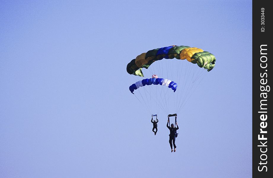 Landing of two parachutes looking like twins on blue sky.