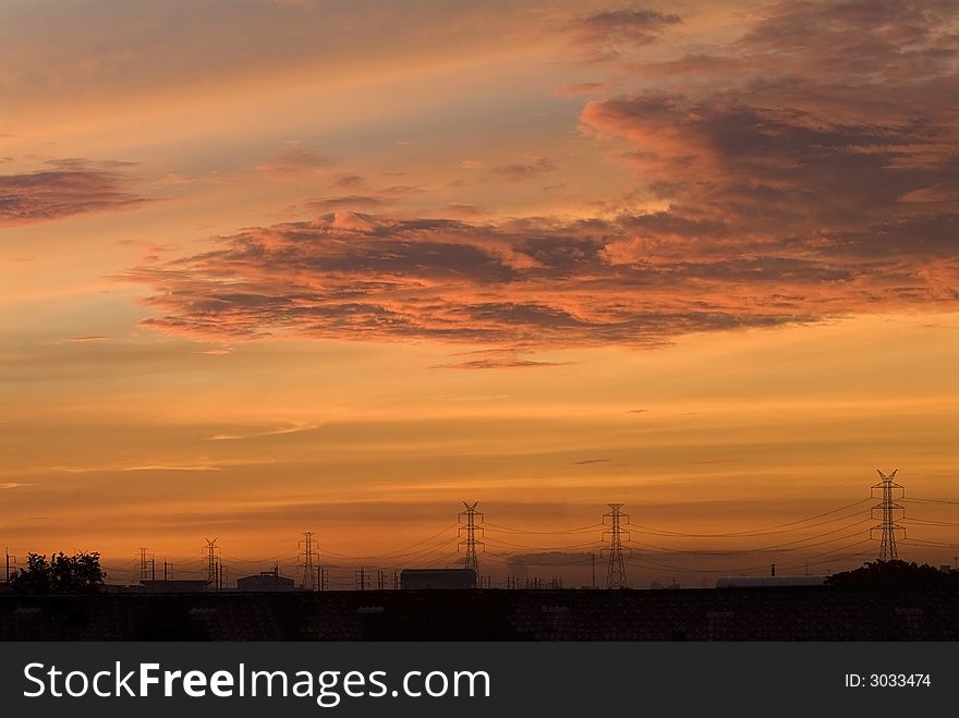 Sunrise in an industrial setting, with the silhouettes of power lines and industrial buildings. Sunrise in an industrial setting, with the silhouettes of power lines and industrial buildings.