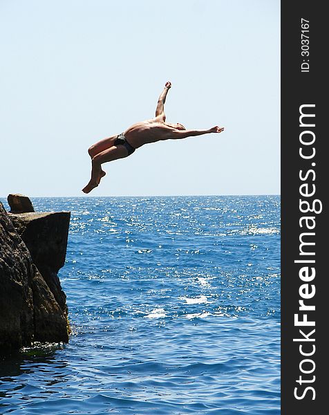 Man making a flip from the rock to the water. Man making a flip from the rock to the water