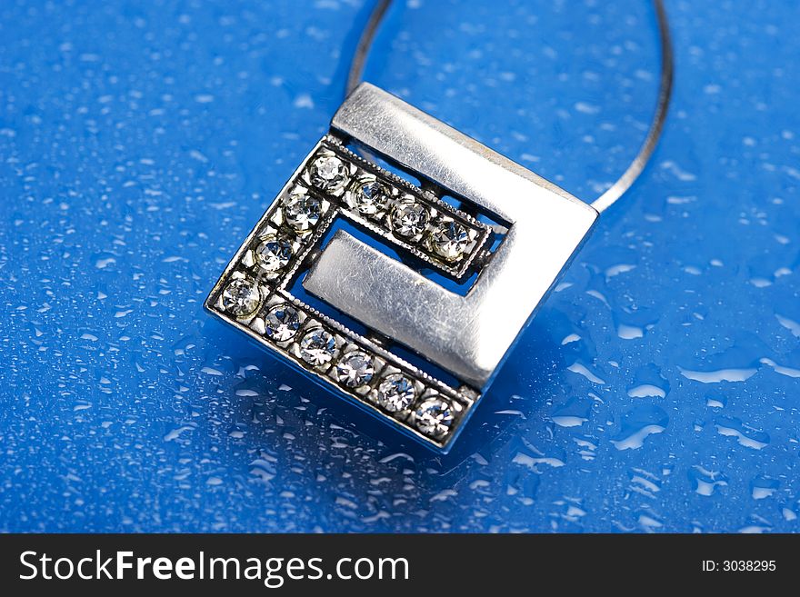 Beautiful silver necklace with diamonds on blue background with water drops