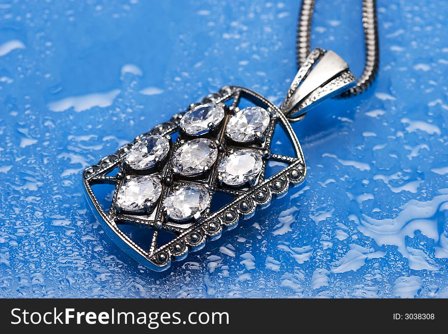 Beautiful silver necklace with diamonds on blue background with water drops. Beautiful silver necklace with diamonds on blue background with water drops