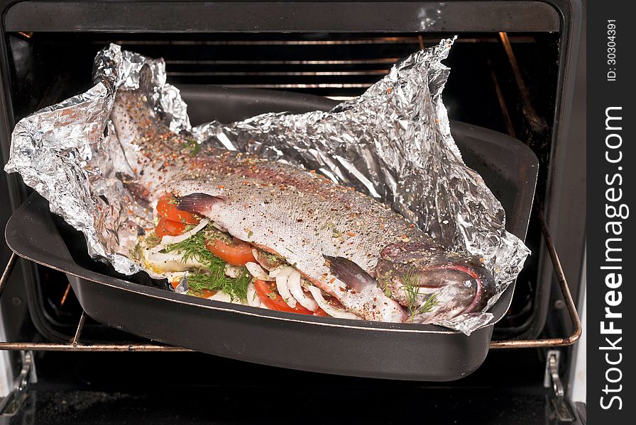 Rainbow trout with vegetable in foil on the metal cookie sheet in the open oven
