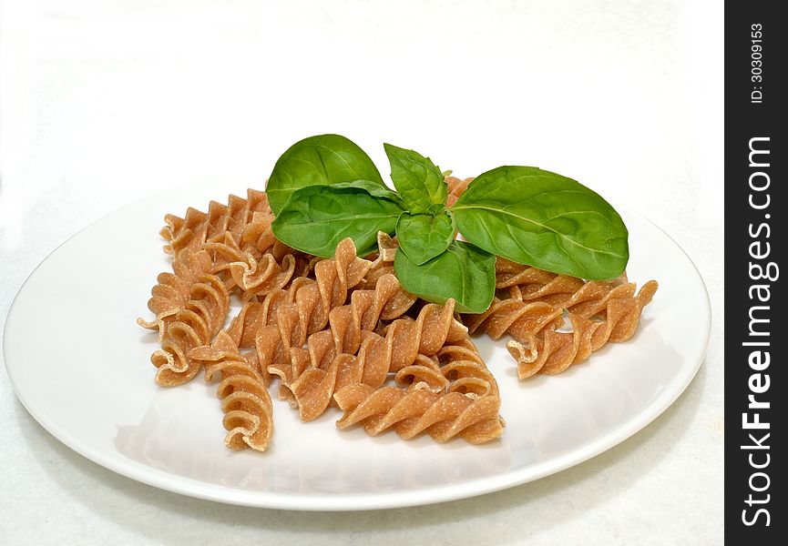 Basil leaves resting on a plate of whole wheat pasta. Basil leaves resting on a plate of whole wheat pasta.