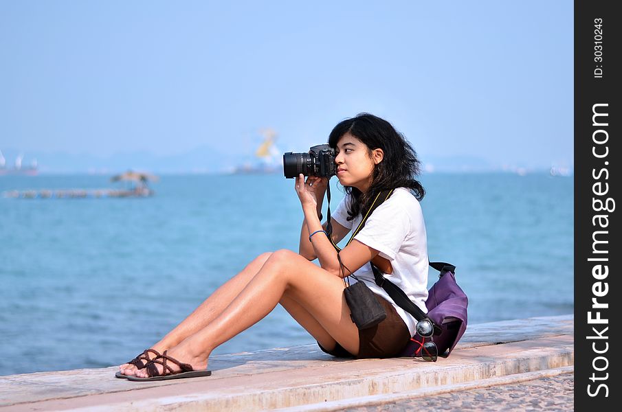 Beautiful young female photographer taking pictures on beach