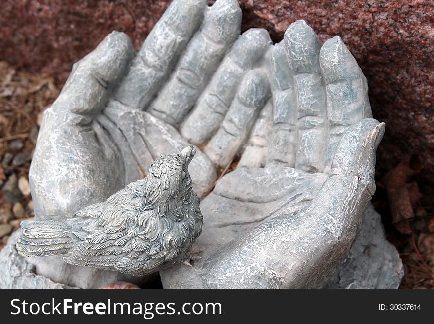 Sculpture of old,weathered stone hands open and holding little bird in palm.