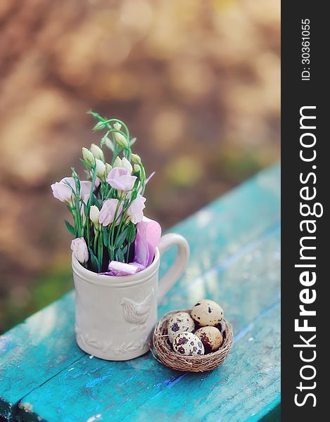 Quail eggs in the nest and a cup with flowers on a blue bench. Quail eggs in the nest and a cup with flowers on a blue bench