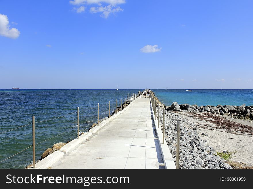 Jetty pier with many people on it and a variety of boats traveling in the Atlantic Ocean water leading to the entrance of Port Everglades in Dania Beach, Florida. Jetty pier with many people on it and a variety of boats traveling in the Atlantic Ocean water leading to the entrance of Port Everglades in Dania Beach, Florida.