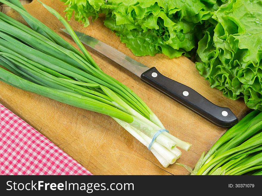 Green onion, knife, lettuce, ramson on the board. Green onion, knife, lettuce, ramson on the board