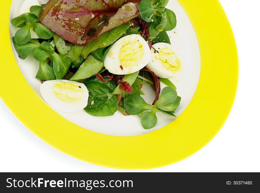 Salad with Greens, Chard, Quail Eggs and Corn Salad on Yellow Plate closeup on white background. Salad with Greens, Chard, Quail Eggs and Corn Salad on Yellow Plate closeup on white background