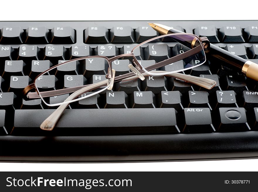 Pen with a golden feather and glasses is on the black keyboard