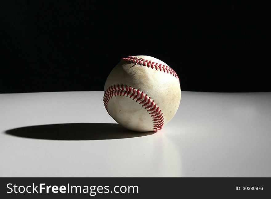 Old dirty baseball isolated on a white table with black background with dramatic lighting. Old dirty baseball isolated on a white table with black background with dramatic lighting