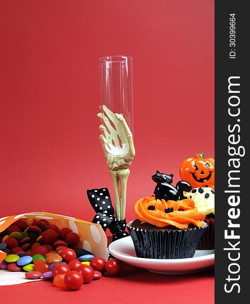 Halloween cupcakes, skeleton glass and candy treats on red background - vertical.