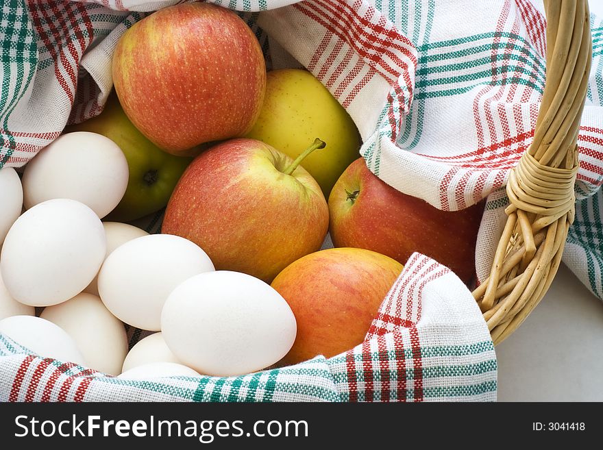 Apples and eggs in a basket with red and green tablecloth