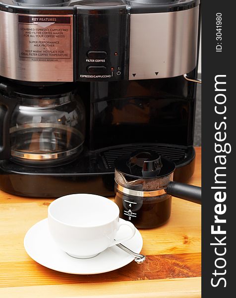 White cup with coffee machine and a freshly brewed pot of coffee in the background. White cup with coffee machine and a freshly brewed pot of coffee in the background