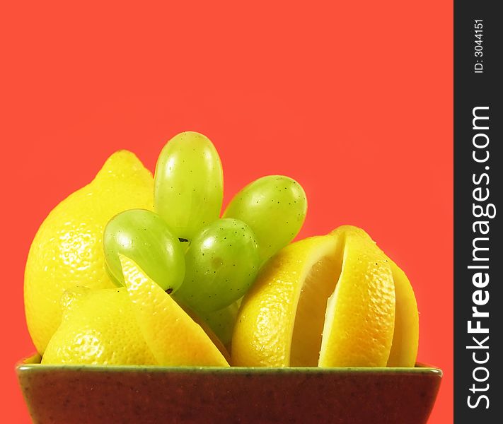 Lemons and grapes fruit in green bowl on red background