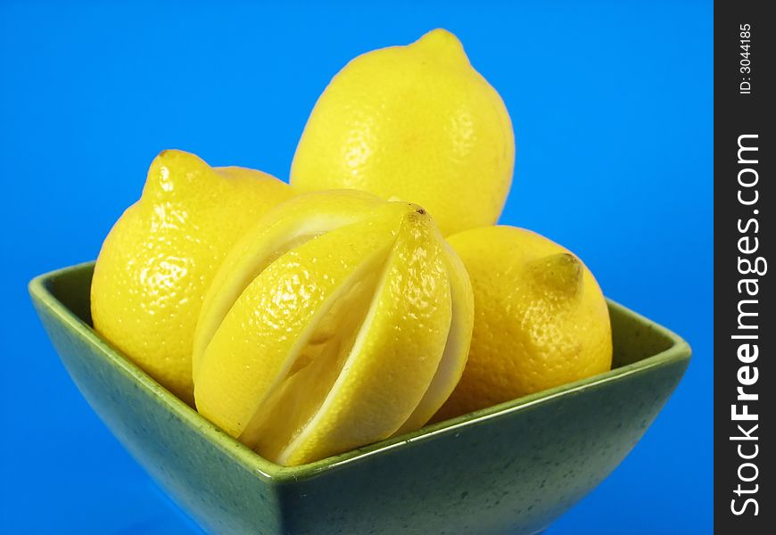 Citrus fruits: lemons in green bowl on blue background. Citrus fruits: lemons in green bowl on blue background