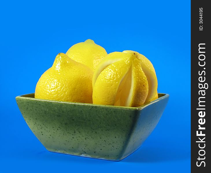 Citrus fruits: lemons in green bowl on blue background. Citrus fruits: lemons in green bowl on blue background